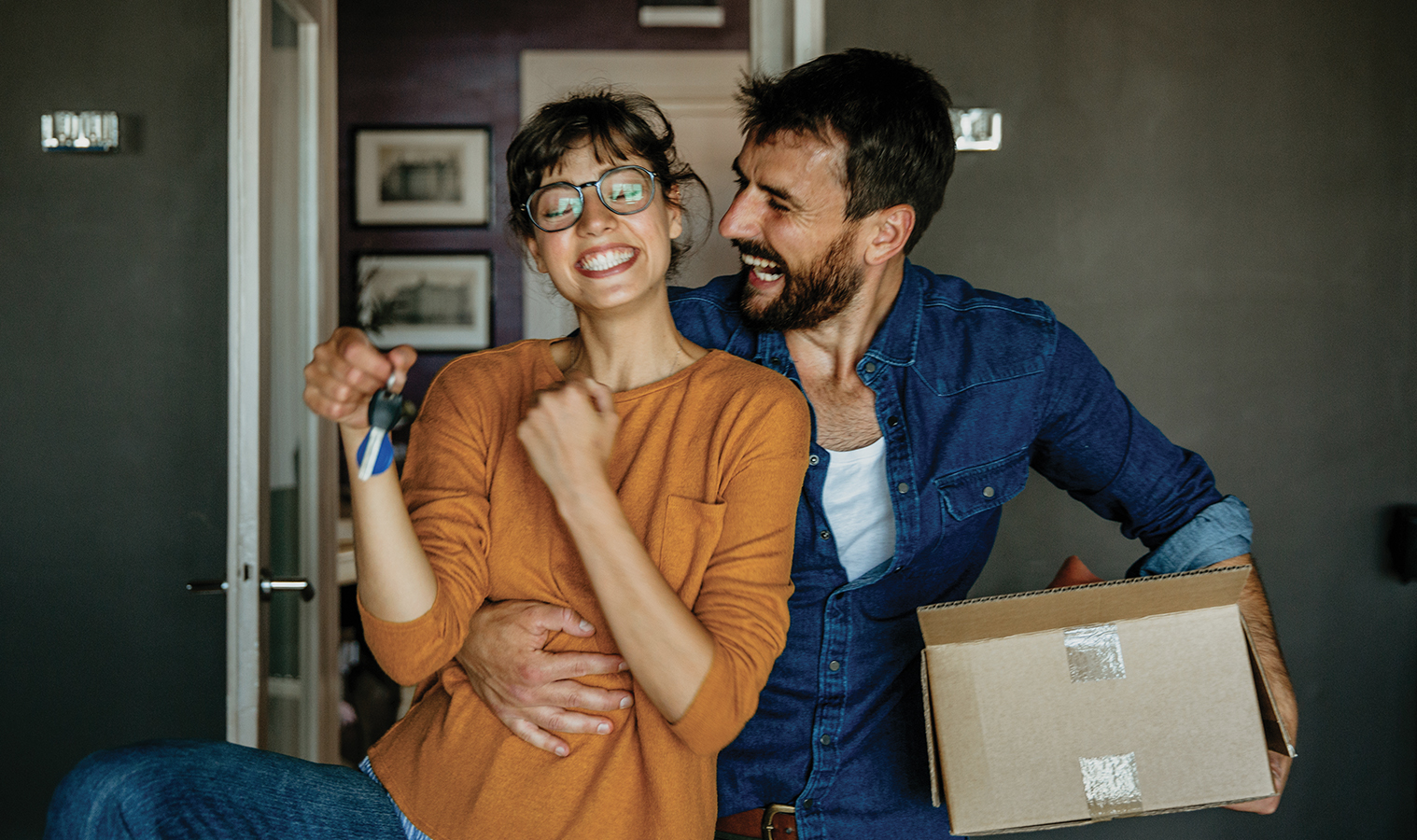 A couple excited to move into their new home. The woman is holding the new house keys, and the man is holding a carboard box.