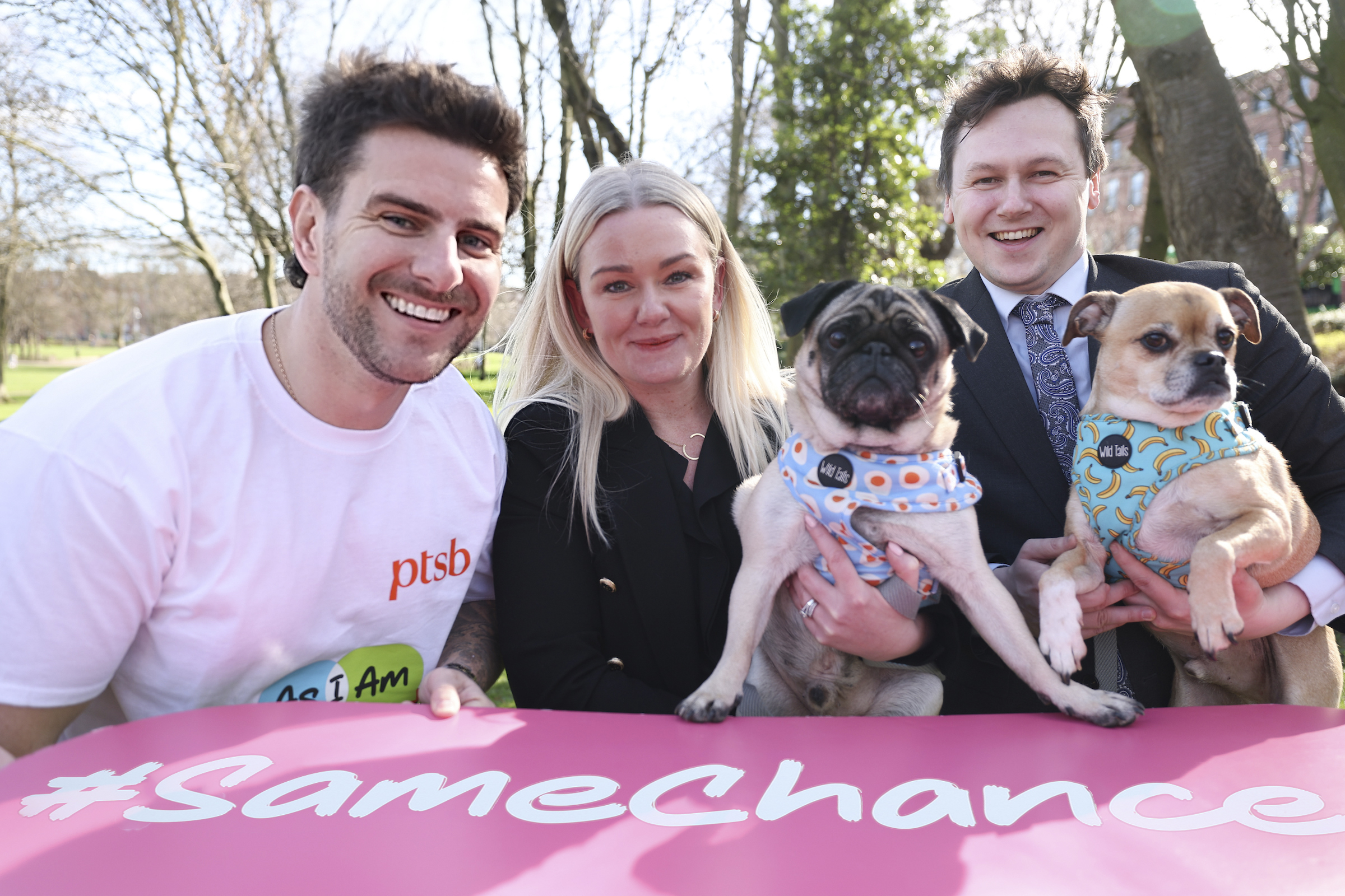 3 people, holding 2 small dogs and a banner with text #same chance