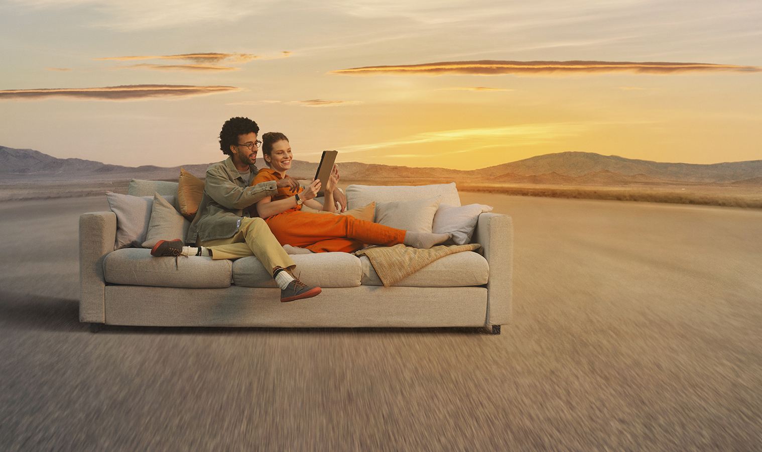 Couple laying comfortably on a sofa in a desert looking at a mobile phone