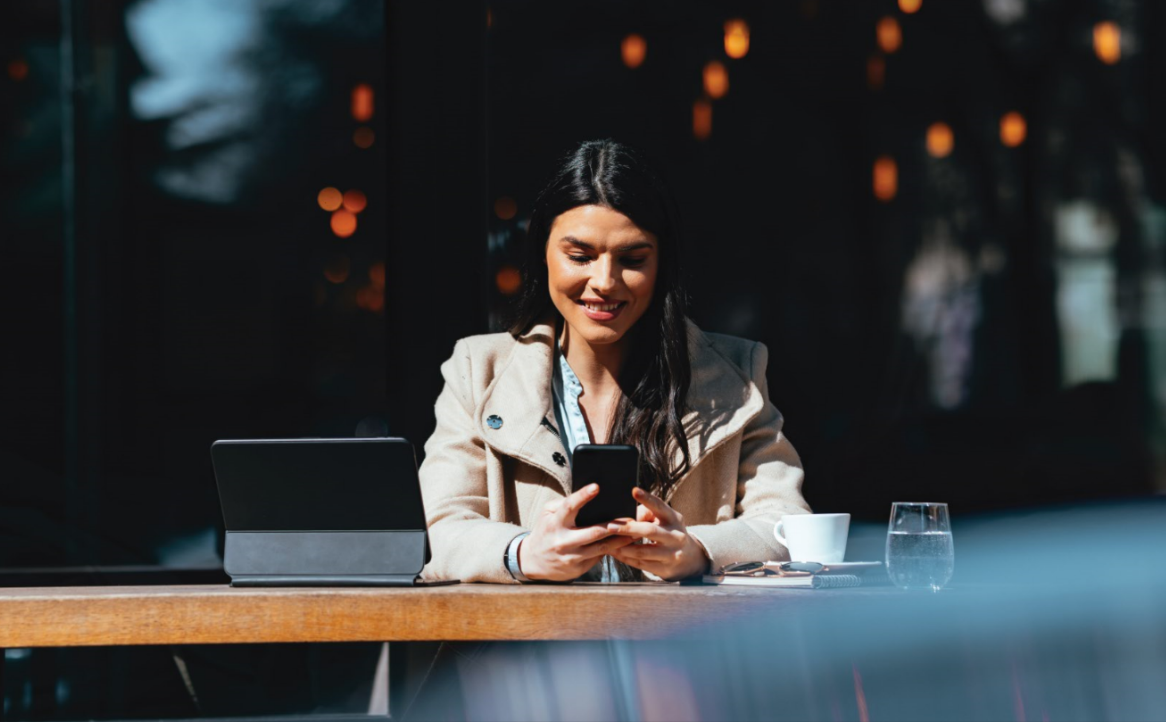 A lady sitting outside a coffee shop browsing the PTSB Mobile App
